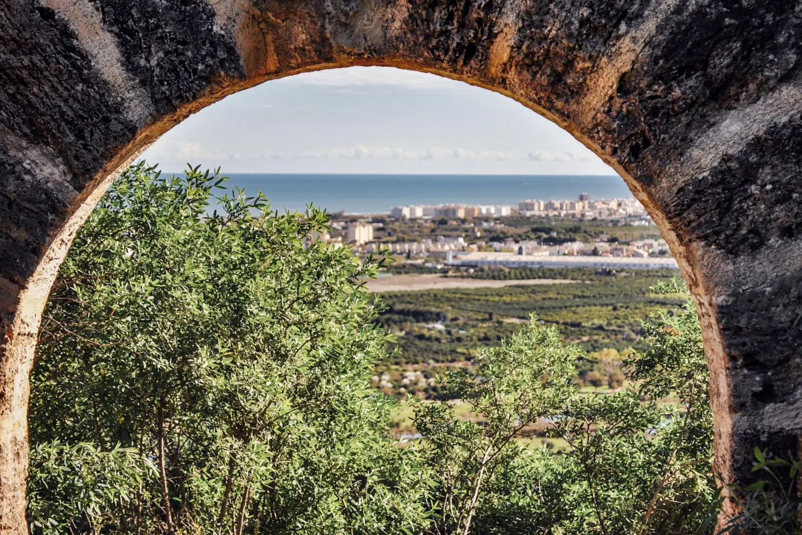 La huerta de Gandia, la ciudad y el mar vistos a través de un arco del Castillo de Bairén