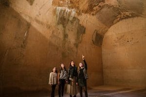 Une femme et trois filles regardent et montrent le plafond voûté à l'intérieur d'une salle d'un bâtiment historique.