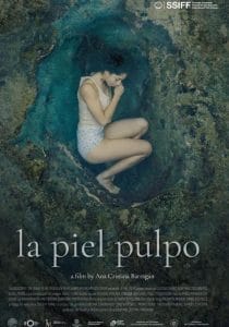 Cartel de la película 'La piel pulpo', de Ana Cristina Barragán: una mujer sentada dentro de una cueva rocosa.