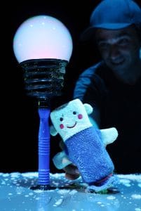 Official image for “En els núvols”: a glowing bubble beside a blue fabric puppet on stage, with a performer in the background.