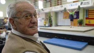 Portrait of Antonio Climent «Misteri» smiling; in the background, weightlifting practice in a sports hall.